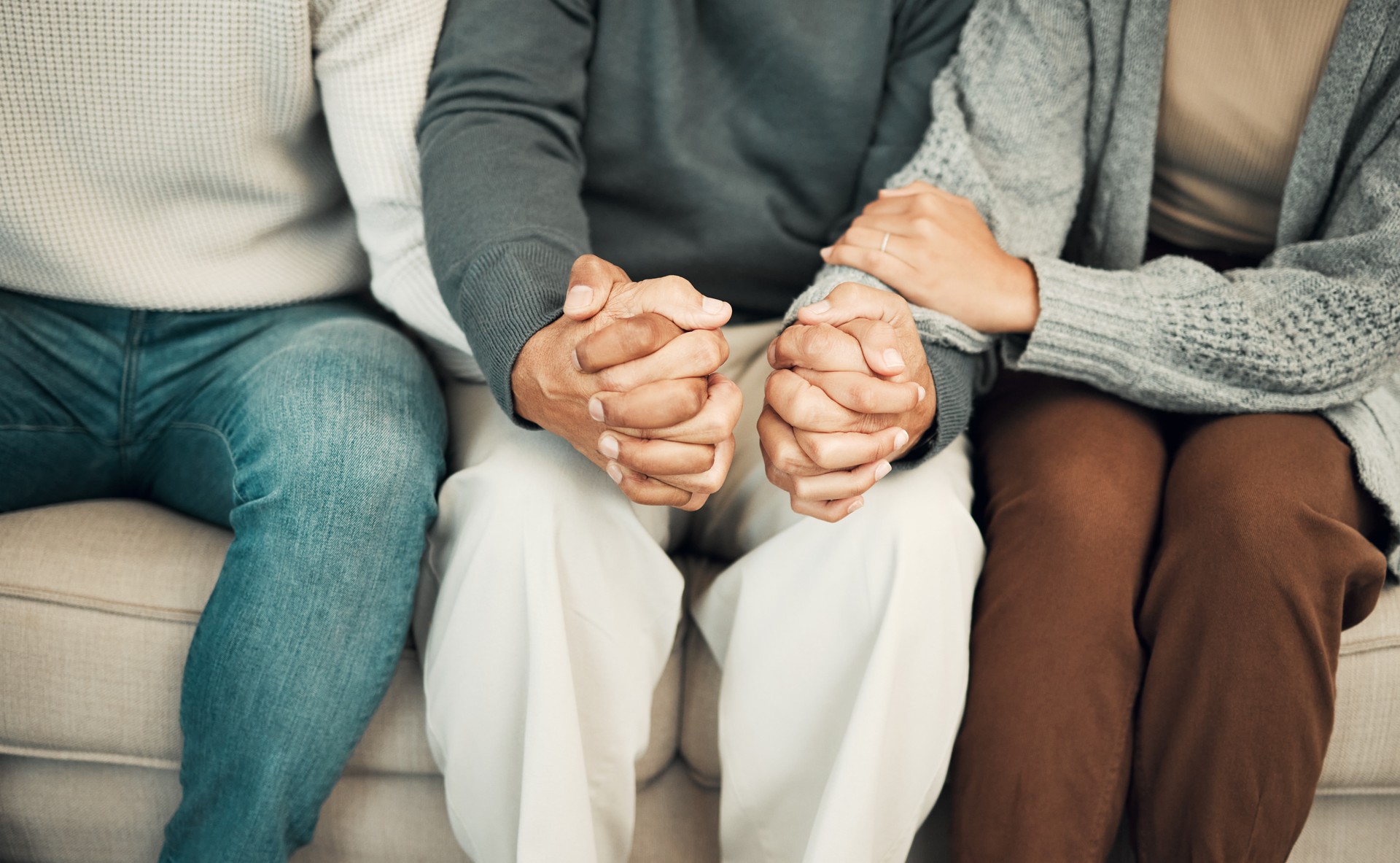 Trust, love and family holding hands on sofa for comforting embrace, prayer and support together at home. Solidarity, empathy and connected parents and adult children for care, compassion and praying