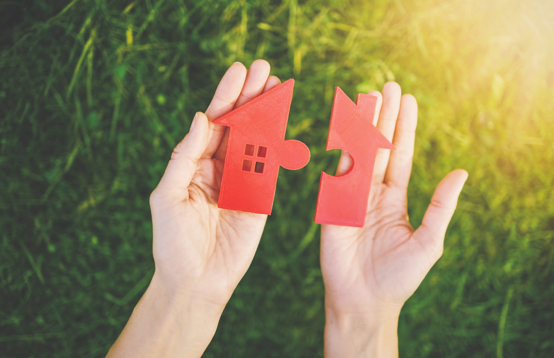 Red house with a shape of two parts of puzzle in human hands.